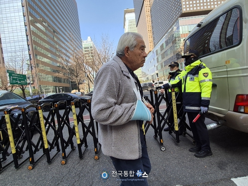 불편한 오른손을 보호대에 의지하고 왼손에는 태극기와 성조기를 들고 광화문 집회 현장을 지키고 있는 시민이 경찰앞을 지나고 있다 / 김경옥 기자